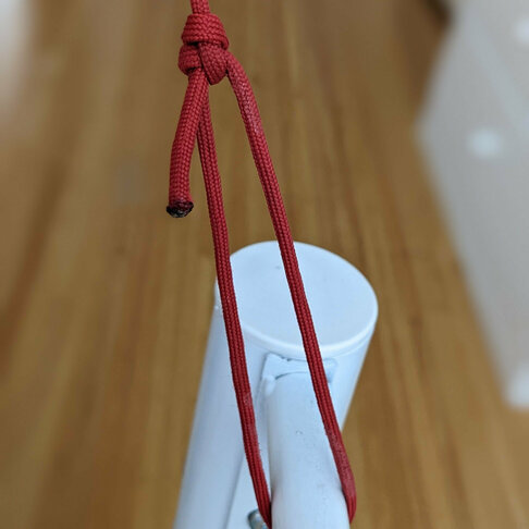 A length of red paracord held taught and looped around a white metal tube.