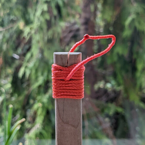 A wooden handle with red cord wrapped tightly around it. The cord tucks beneath itself to form a dangling loop.