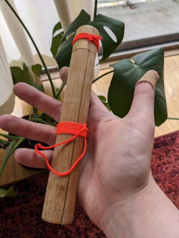 A bamboo toothbrush case that has split into halves, bound back together with thin fluorescent string around its base and cap. The loose ends of the whipping around the body have been melted together to form a closed loop.