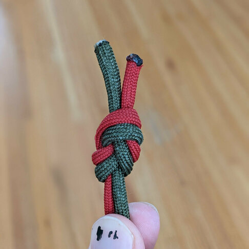 A pair of green and red paracord lengths knotted together to form a single cord.